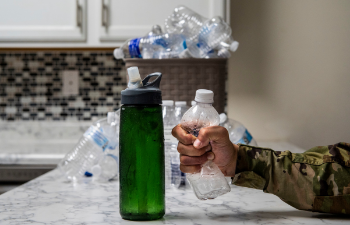 Image of soldier crushing a plastic water bottle in his hand, with a reusable water bottle on the counter