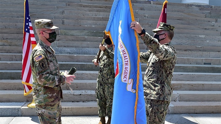 Army Lt. Gen. Ronald Place, director of the Defense Health Agency, left, and Navy Rear Adm. Darin Via, director of the Tidewater Market, and commander, Naval Medical Forces Atlantic, unfurl the Defense Health Agency flag during a socially distanced establishment ceremony to mark the standup of the Tidewater Market, April 28, 2021. Tidewater Market is on the leading edge of the Military Health System’s historic change, following its certification by the Defense Health Agency on April 19, 2021 (Photo by: Navy Petty Officer 2nd Class Jessica Dowell, Naval Medical Forces Atlantic).