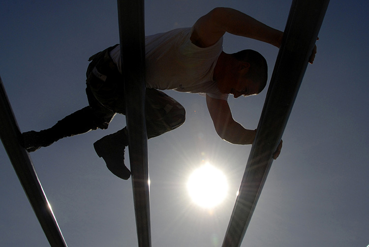 Image of A U.S. Navy Basic Underwater Demolition/SEAL student moves through the weaver during an obstacle course session. Click to open a larger version of the image.