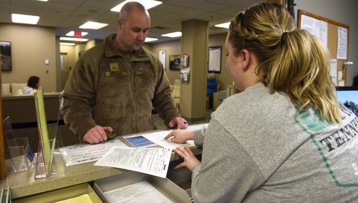 Image of Military personnel at desk assisting an Airman with paperwork.