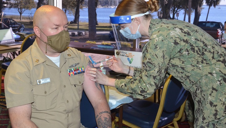 Image of Military health personnel wearing a face mask and a face shield giving the COVID-19 vaccine. Click to open a larger version of the image.
