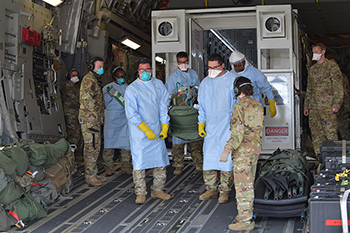 Military medical personnel, wearing masks and gloves, loading a COVID-19 patient into an isolated containment chamber