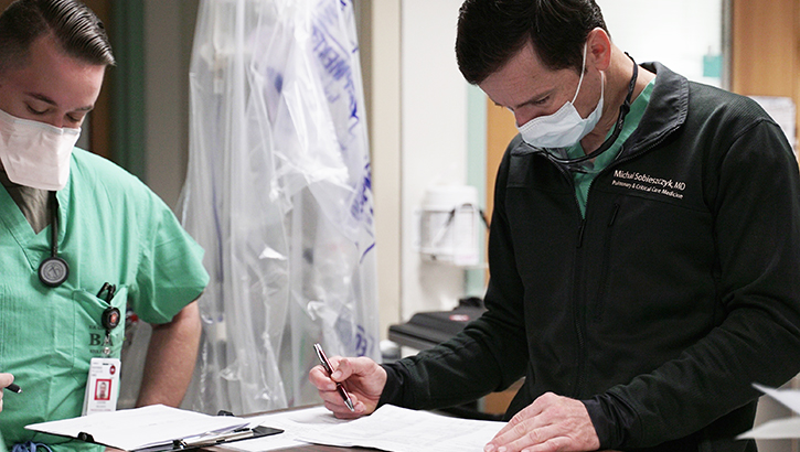 Image of Medical personnel wearing masks, looking at paperwork on desk. Click to open a larger version of the image.
