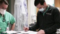 Medical personnel wearing masks, looking at paperwork on desk