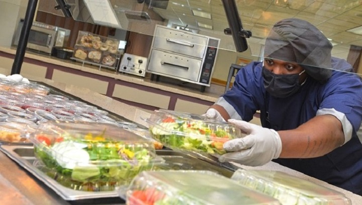Image of Man wearing mask and gloves putting container of salad into salad bar.