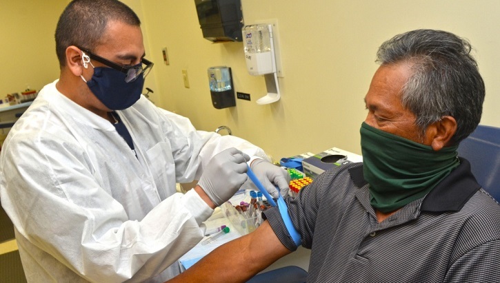 Image of Medical technician giving a man a vaccine shot; both wearing masks.