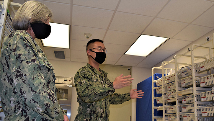 Two military personnel, wearing masks, in a supply room looking at the shelves