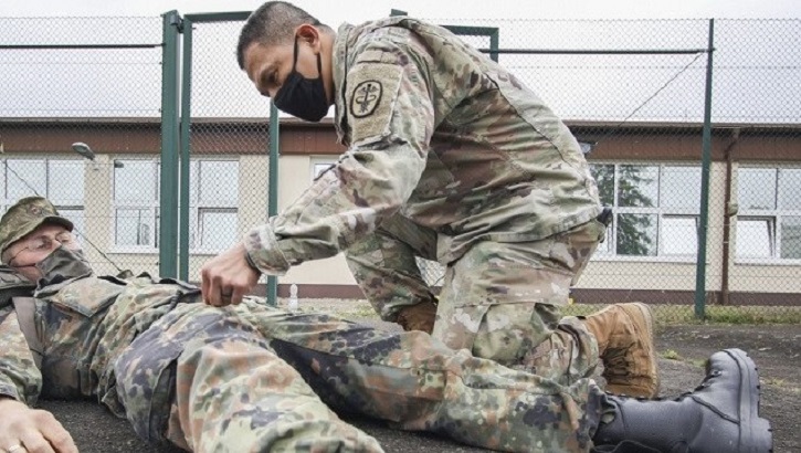 Two soldiers, one laying on the ground and the other giving him medical attention