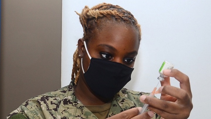 Image of Military personnel, wearing a mask, looking at a syringe and a vial.