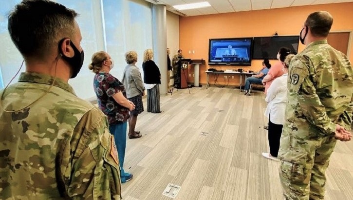 Image of Military personnel standing in a room, listening to a speaker. Click to open a larger version of the image.
