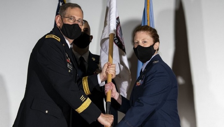 Two military personnel wearing masks, holding onto a flag