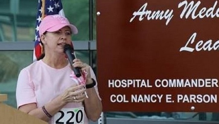 Image of Woman in pink hat and shirt, wearing a racing number, speaking to an audience.