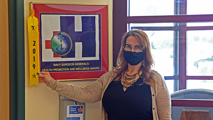 Image of Woman wearing a mask, pointing to an award ribbon.