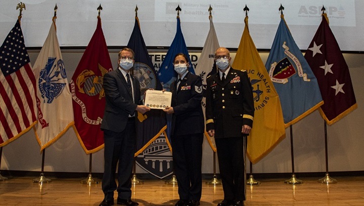 Image of Three military personnel in uniform, wearing masks, in front of flags.