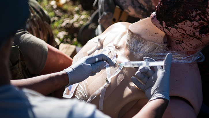 Image of Military personnel participating in training exercise, treat a dummy for injuries.