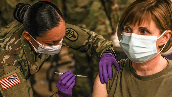 Image of military personnel giving a vaccine to a soldier in her right arm. Click to open a larger version of the image. Click to open a larger version of the image.