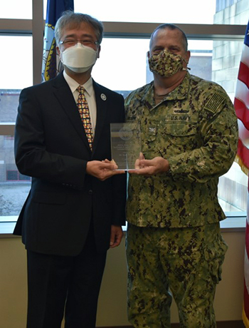 Two men, wearing masks, holding onto a glass award