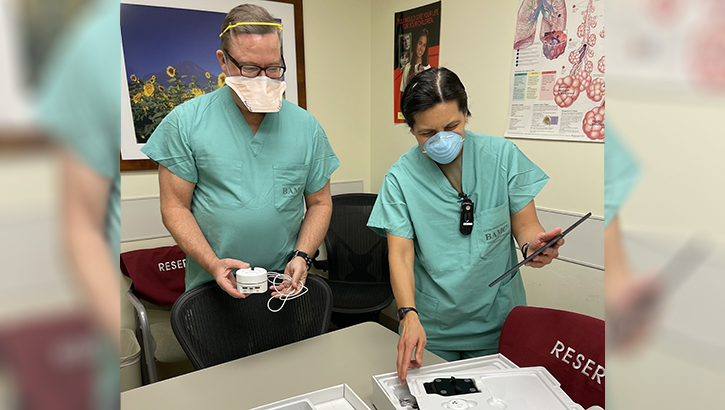 Image of two medical personnel, wearing masks, looking at the contents of a home-based COVID treatment kit. Click to open a larger version of the image. Click to open a larger version of the image.