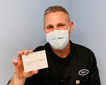 Medical personnel, wearing a mask, shows his vaccination card