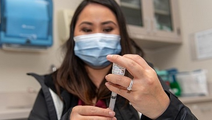 Image of a military healthcare worker holding a vaccine needle. Click to open a larger version of the image. Click to open a larger version of the image.