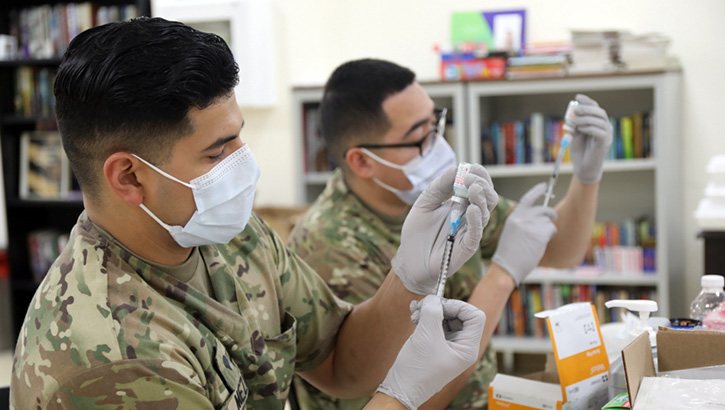 Image of Two healthcare workers, wearing masks, adding the COVID-19 vaccine to syringes.