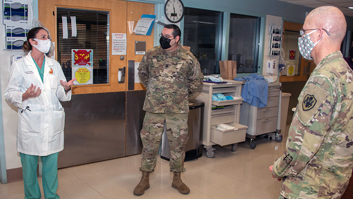 Three military personnel, wearing masks, talking with each other in a hospital hallway
