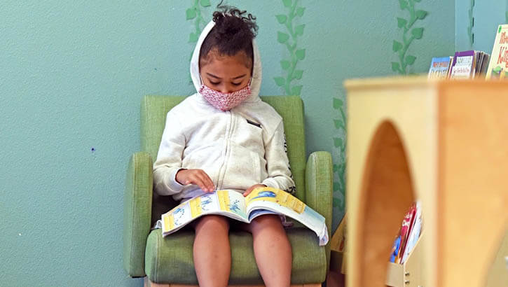 5-year-old girl in mask reads a book by herself
