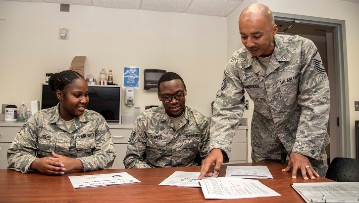 Image of Three soldiers at a desk, two sitting and one standing, pointing at a piece of paper. Click to open a larger version of the image.
