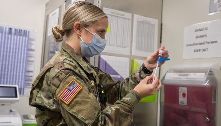 Image of a military nurse, wearing a mask, preparing a needle for a vaccination. Click to open a larger version of the image.