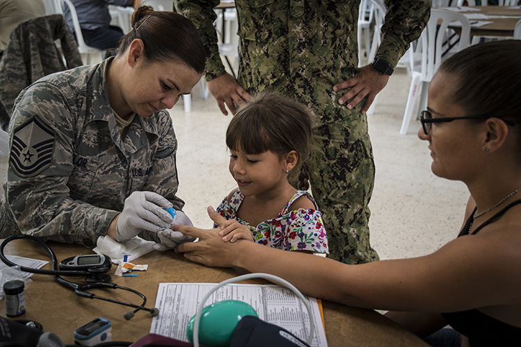 Master Sgt. Tara Taylor performs a glucose checks wile a young girl consoles her mother. (U.S. Air National Guard photo by Staff Sgt. Bethany Rizor)