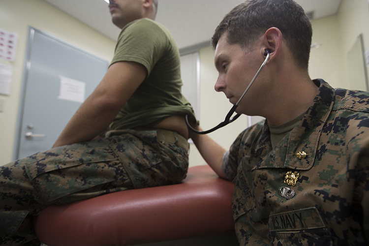 Image of A U.S. naval officer listens through his stethoscope to hear his patient’s lungs. Click to open a larger version of the image.