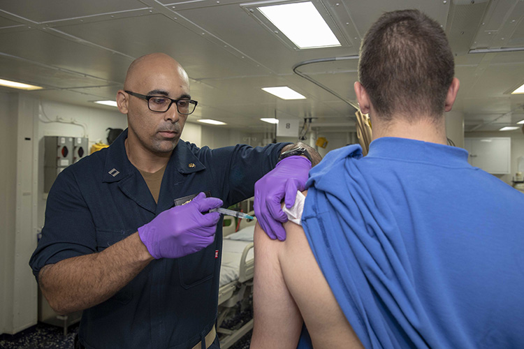 Image of Lt. Sipriano Marte administers an influenza vaccination to Airman Tyler French. Click to open a larger version of the image.