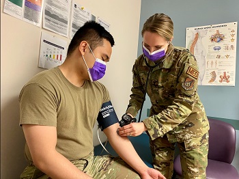 Military health personnel wearing a face mask checking the blood pressure of a patient