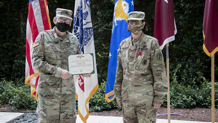 Image of Two masked soldier display an award in front of flags.