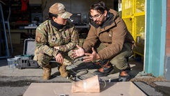 Andres Martinez Murillo, lead biomedical engineer for Naval Medical Research Unit (NAMRU) San Antonio, explains stability testing on the novel SynDaver thermal, bleeding manikin thigh to U.S. Air Force Lt. Col. Kaitlin Salle at the Kodiak Coast Guard Clinic