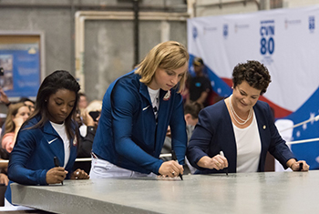 Biles, Ledecky, and Boykin signing a 35-ton steel plate
