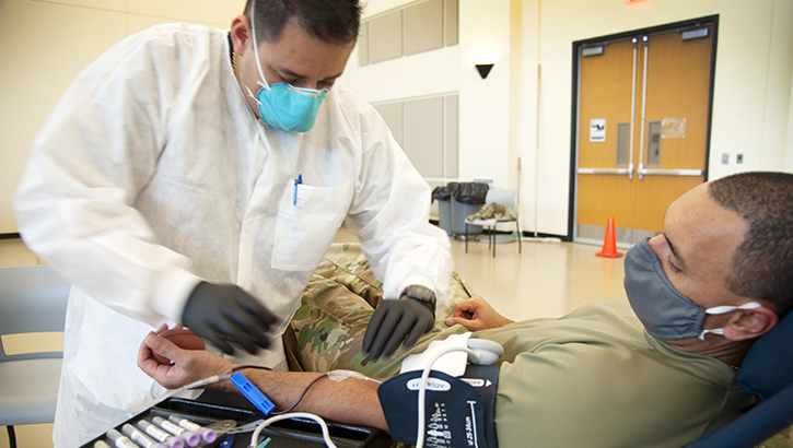 Service member gives blood while wearing a mask.