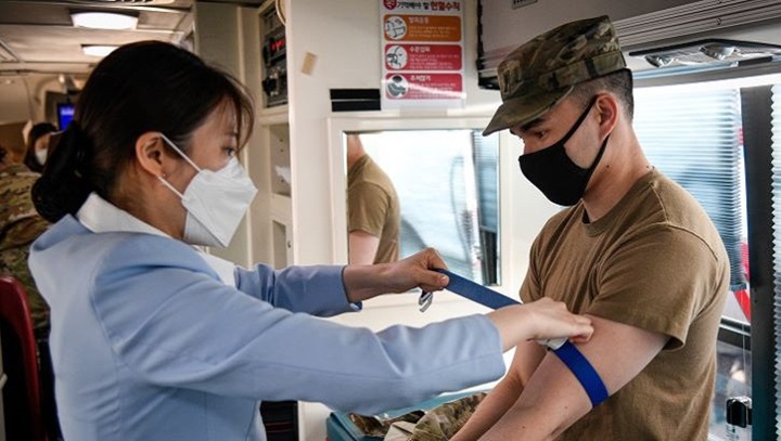 Image of Military personnel wearing a face mask drawing blood during a blood drive.