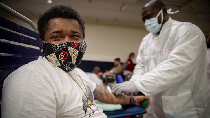 Image of Military health personnel wearing a mask drawing blood from military personnel wearing a mask.