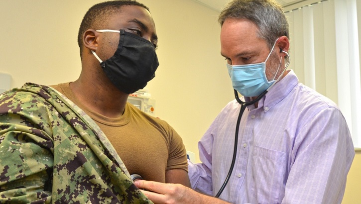 Military personnel wearing a face mask, gets his heart checked out by military heath personnel