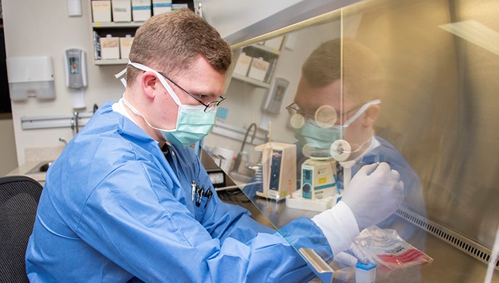 Image of Man in lab coat and mask prepares sample for COVID-19 testing. Click to open a larger version of the image.