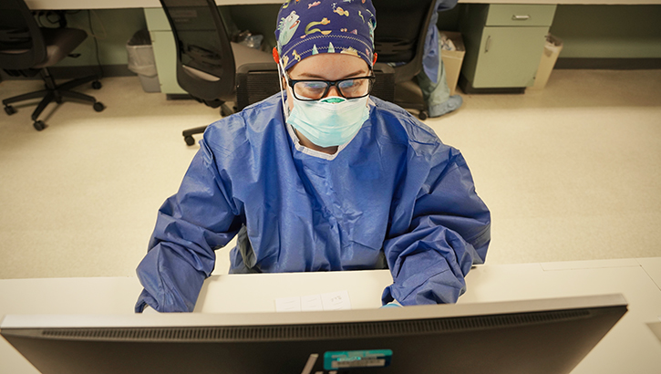 Image of Clinician with mask looks at computer screen at a hospital. Click to open a larger version of the image.
