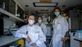 Three military personnel, wearing masks and lab coats, pose for a picture in an Albanian lab.