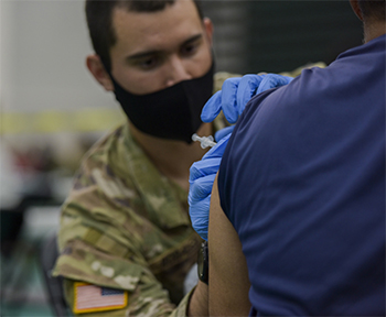Military health personnel wearing a face mask administering the COVID-19 vaccine
