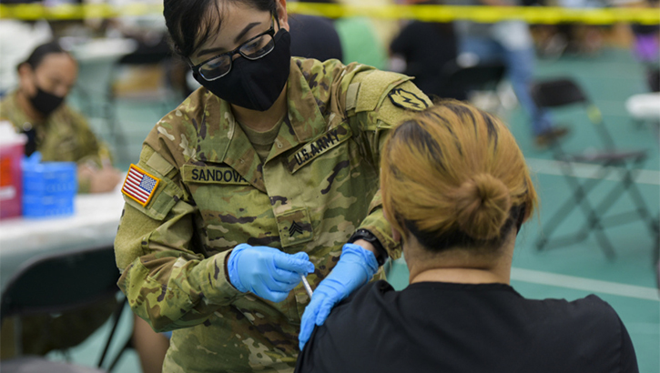 Military health personnel wearing a face mask administering the COVID-19 vaccine