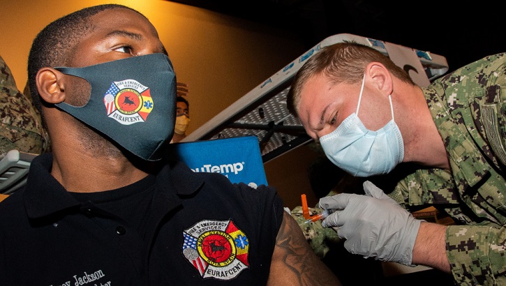 Image of two soldiers, wearing masks: one is getting a vaccine in his left arm. Click to open a larger version of the image.