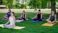 Five people sitting on yoga mats outside in the grass