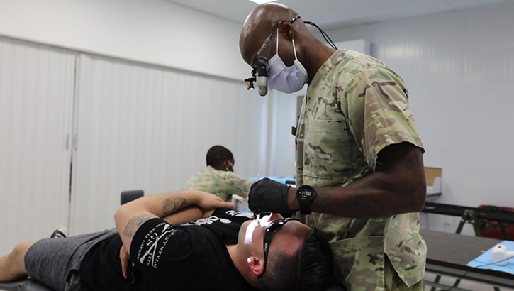Military health personnel wearing a face mask looking at someone's teeth
