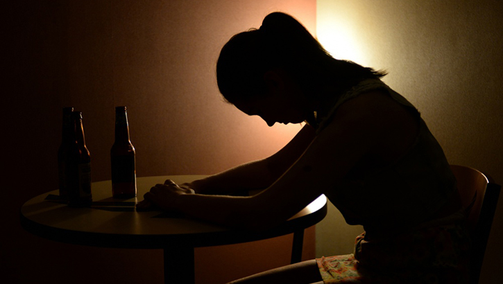 Image of Shadowed image of person sitting at a desk with their head down.