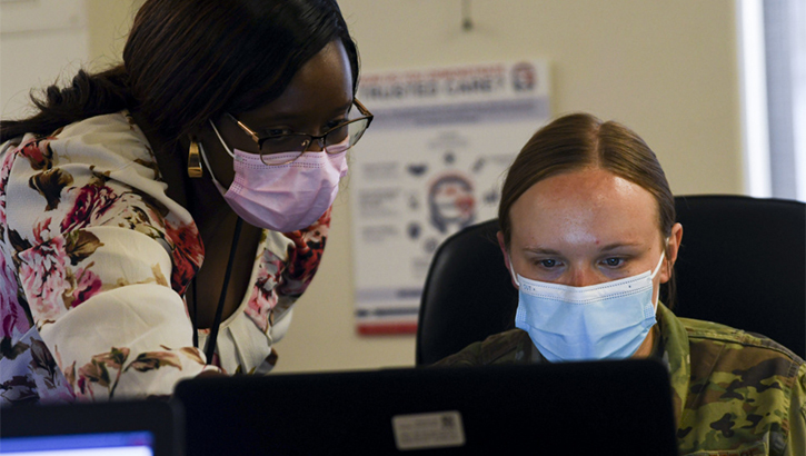 Image of Military health personnel wearing face mask looking at  a computer. Click to open a larger version of the image.